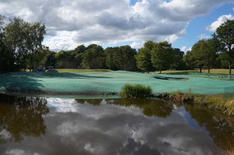 Hydroseeded golf course reflected in pond with machinery in background